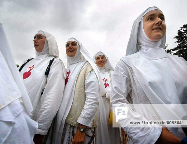 'Lourdes  visit of Pope Benedict XVI (2008/09/13) : young nuns from the congregation of ''Les soeurs de la consolation'' wearing white tunicles (dresses) ornated with the red Sacred Heart and a cross  and French flags. 2008 is the year of the 150th anniversary of Virgin Mary's apparition to Bernadette Soubirous. Pilgrimage  pilgrim  nun  sister  tunicle  Catholic religion'