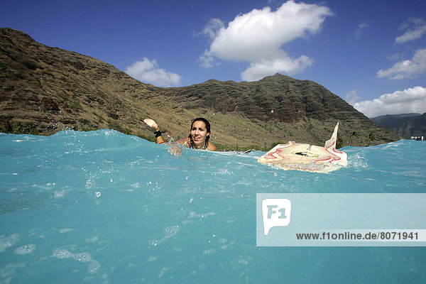 Hawai (Hawaii): Surfing. Young surfer with brown hair  in the water  next to her surfboard  and mountains in the background