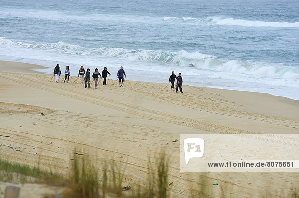 'Group of people practicing nordic walking on a beach of Mimizan (40) in the Landes department with the association called ''Nordicevasion''. . Nordic walking in the sand with walking poles'