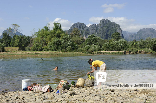 Laotische Frauen waschen Wäsche am Fluss Nam Khan  hinten das Karstgebirge