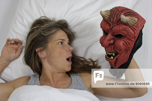 Frau liegt im Bett  Teufelsmaske