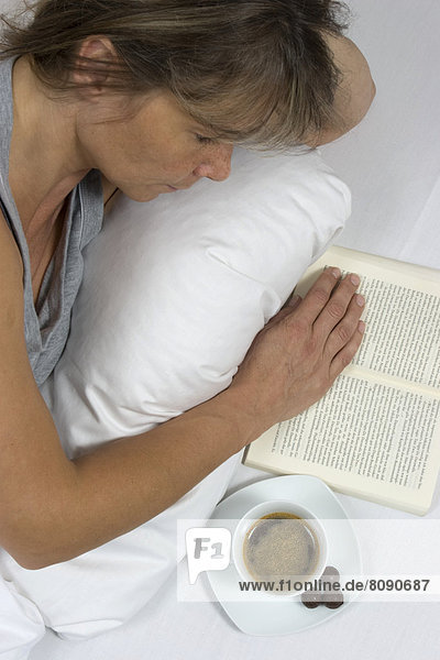 Frau liest ein Buch im Bett  Kaffeetasse