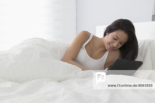 Mixed race woman using tablet computer in bed
