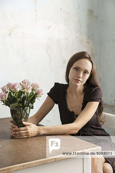 Junge Frau sitzt an Tisch mit Blumenstrauß