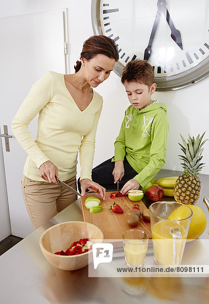 Mutter und Sohn schneiden verschiedene Sorten Obst auf Schneidebrett in Küche