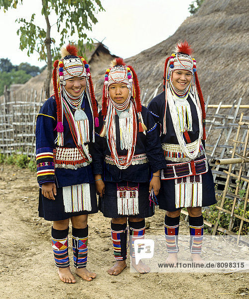 Drei Akha-Mädchen in einem Bergdorf mit traditioneller Kleidung und Kopfbedeckung