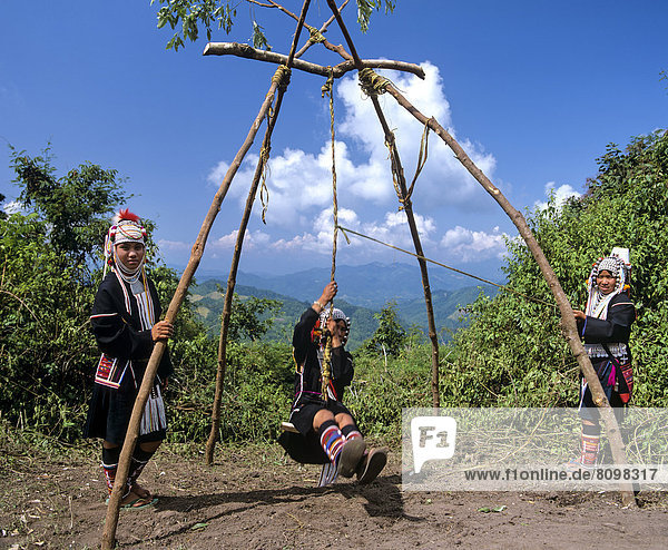 Swing ceremony  a harvest festival ritual  three young Akha girls at a swing in traditional costume and headdress