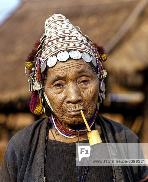 Akha-Frau mit Pfeife  traditioneller Kleidung und Kopfbedeckung mit Silbergmünzen  Portrait
