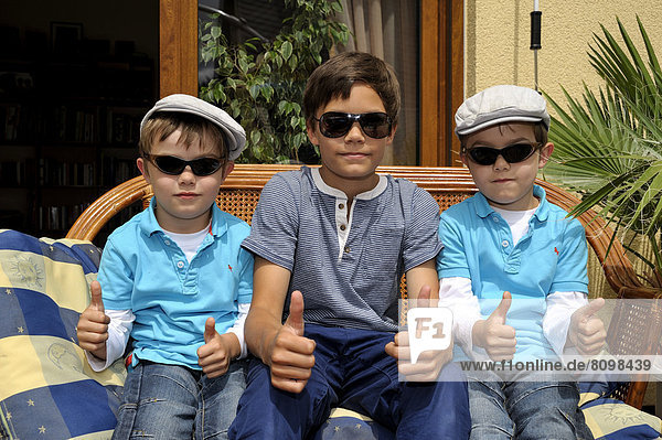 Twins and their older brother sitting together on a bench on a terrace