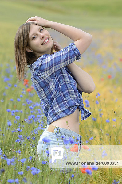 Junge Frau steht in einem Kornblumenfeld