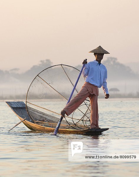Intha 'leg rowing' fishermen at dawn on Inle Lake who row traditional wooden boats using their leg and fish using nets stretched over conical bamboo frames  Inle Lake  Myanmar (Burma)  Southeast Asia