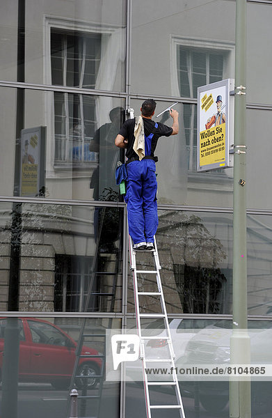 'Glasfassadenreiniger auf Leiter bei der Arbeit  neben Werbebanner ''Wollen Sie nach oben?'''