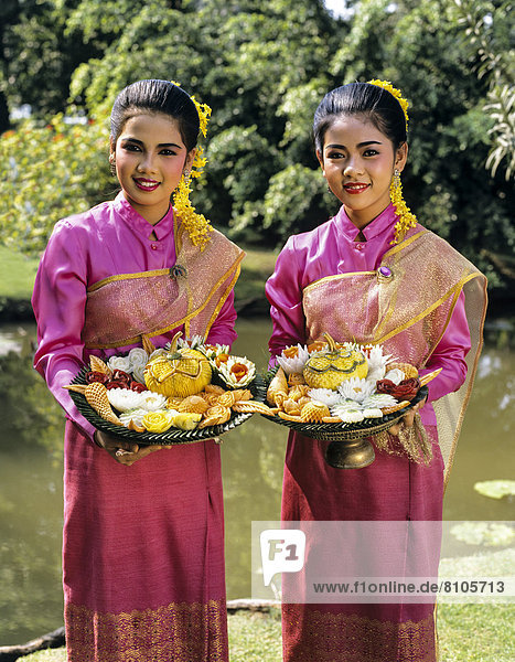 Zwei junge Frauen in traditionellen Kostümen mit geschnitzten exotischen Früchten  Rose Garden