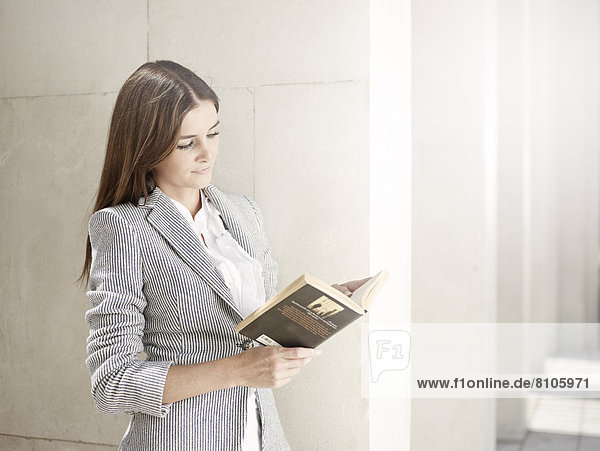 Frau im Business-Outfit lehnt sich an eine Mauer und liest ein Buch