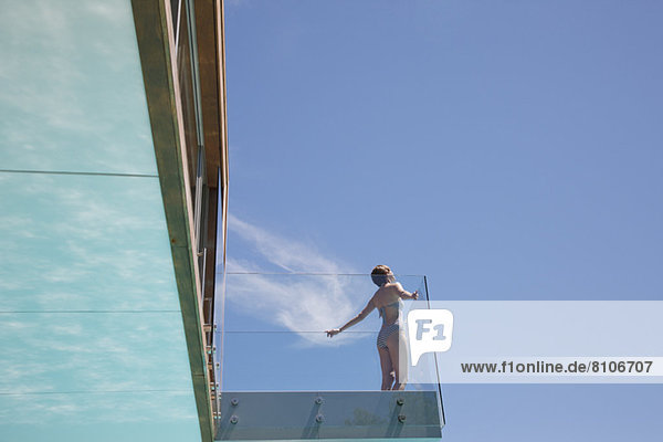 Frau mit ausgestreckten Armen auf modernem Balkon