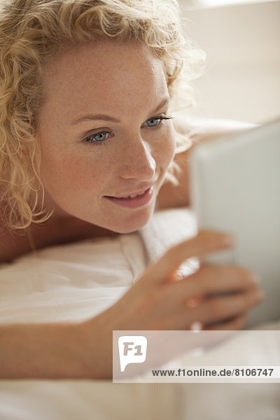 Close up of woman laying in bed using digital tablet