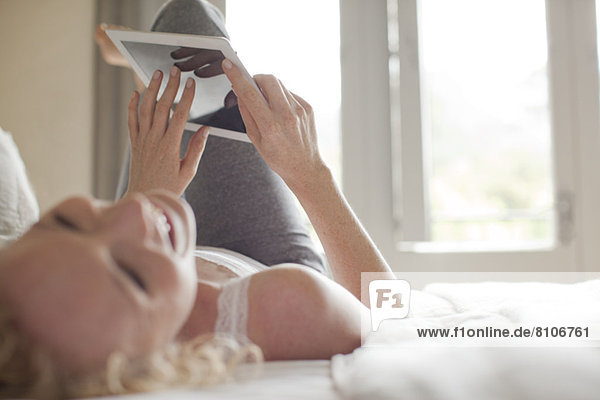 Laughing woman laying in bed using digital tablet
