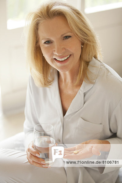 Portrait of smiling woman holding pill and glass of water