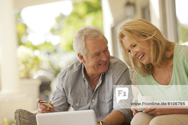 Smiling couple drinking coffee and shopping online on patio