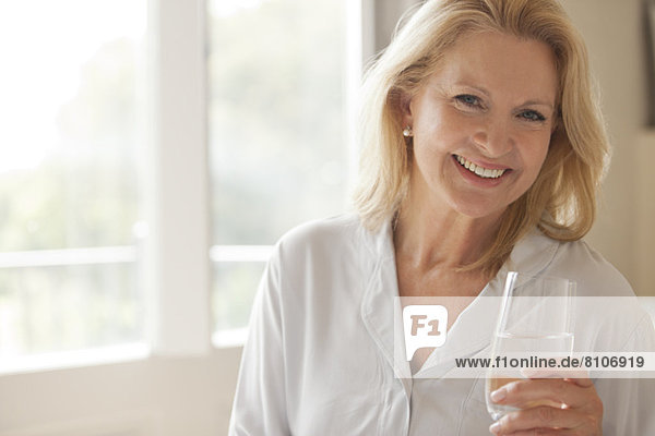 Porträt einer lächelnden Frau  die ein Glas Wasser trinkt.