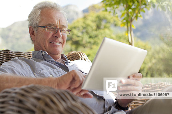Lächelnder älterer Mann mit digitalem Tablett auf der Terrasse