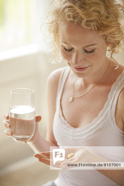 Woman holding glass of water and pills