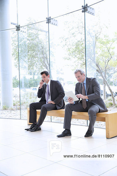 Businessmen using cell phone and digital tablet in lobby