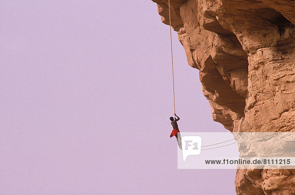 Africa Ireli Sky Mountains Cliffs Rock Uneven Rope One Person One Male Hanging Suspended Climbing Holding Tribal Culture Adventure Challenge Grip Risky Outdoors Day Distant Full Length Side View Horizontal Color Image Photography