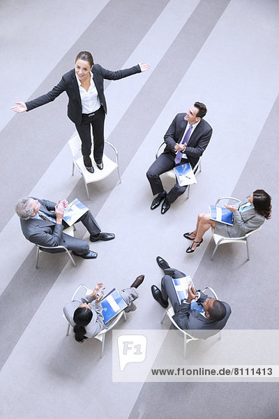 High angle view of businesswoman standing on chair in circle with co-workers