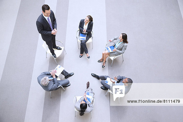 High angle view of businessman standing on chair in circle with co-workers