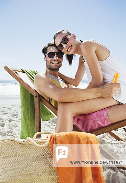 Porträt eines lächelnden Paares mit Sonnencreme auf den Nasen am Strand