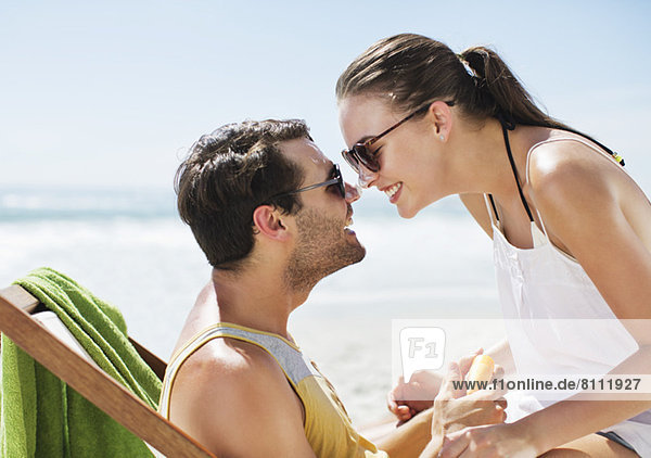 Ein glückliches Paar  das am Strand mit Sonnencreme bedeckte Nasen reibt.