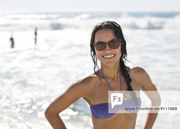 Porträt der lächelnden Frau im Bikini und Sonnenbrille am Strand