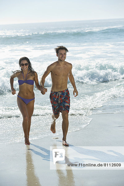 Ein glückliches Paar  das Händchen hält und am Strand rennt.