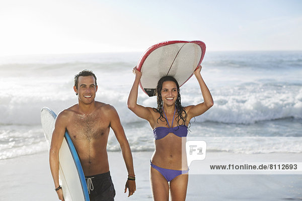 Glückliches Paar mit Surfbrettern am Strand