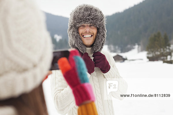 Woman photographing man wearing fur hat in snowy field