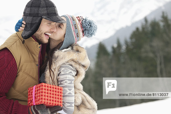 Happy couple with Christmas gift kissing in snowy field