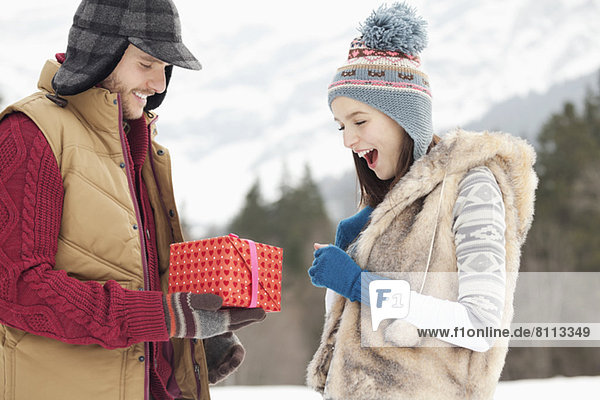 Man surprising woman with gift in snowy field