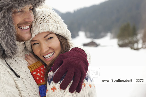 Close up portrait of happy couple hugging in snowy field