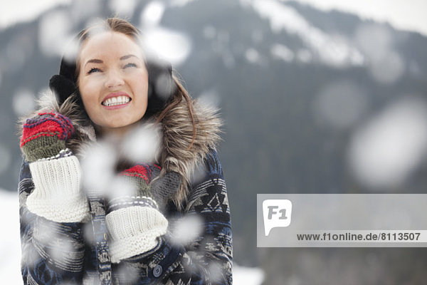 Glückliche Frau mit Ohrenschützern und Handschuhen im Schnee