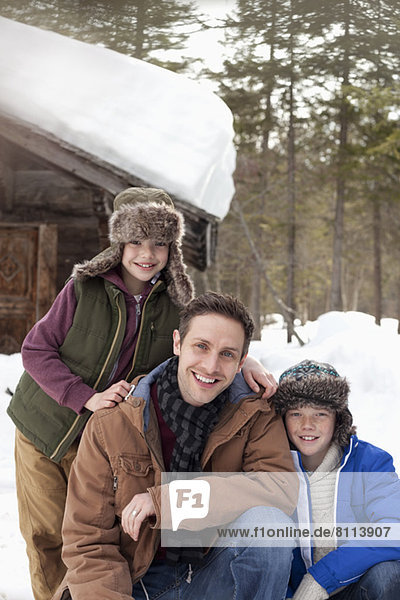 Portrait of smiling father and sons in snow outside cabin