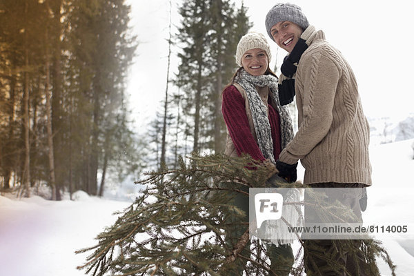 Portrait of happy couple with fresh Christmas tree in snowy woods