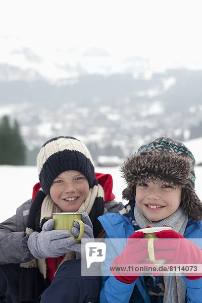 Portrait of smiling boys drinking hot chocolate in snowy field
