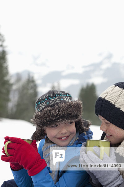 Close up of happy boys drinking hot chocolate in snowy field