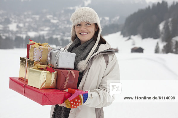 Portrait of smiling woman carrying Christmas gifts in snowy field