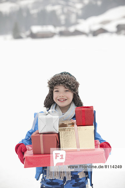 Portrait of smiling boy carrying stack of Christmas gifts in snow