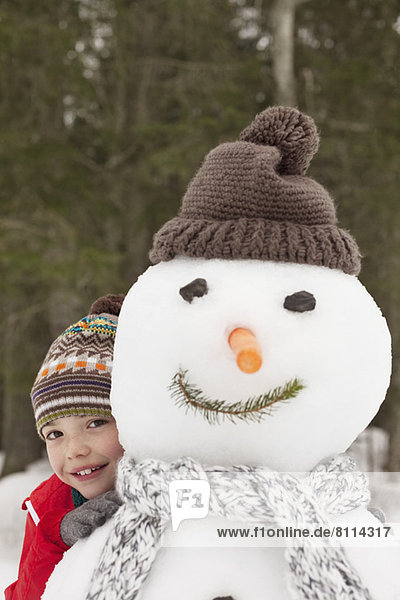 Portrait of smiling boy behind snowman with stocking-cap