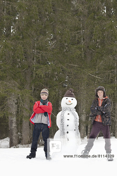 Portrait of confident boys next to snowman in woods