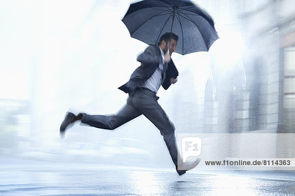 Geschäftsmann mit Regenschirm in der verregneten Straße