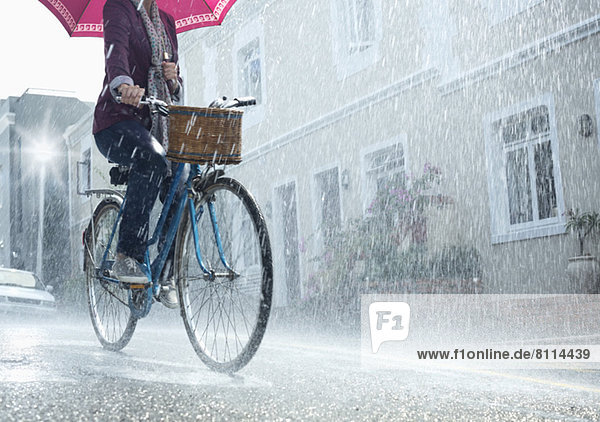 Fahrradfrau mit Regenschirm in verregneter Straße